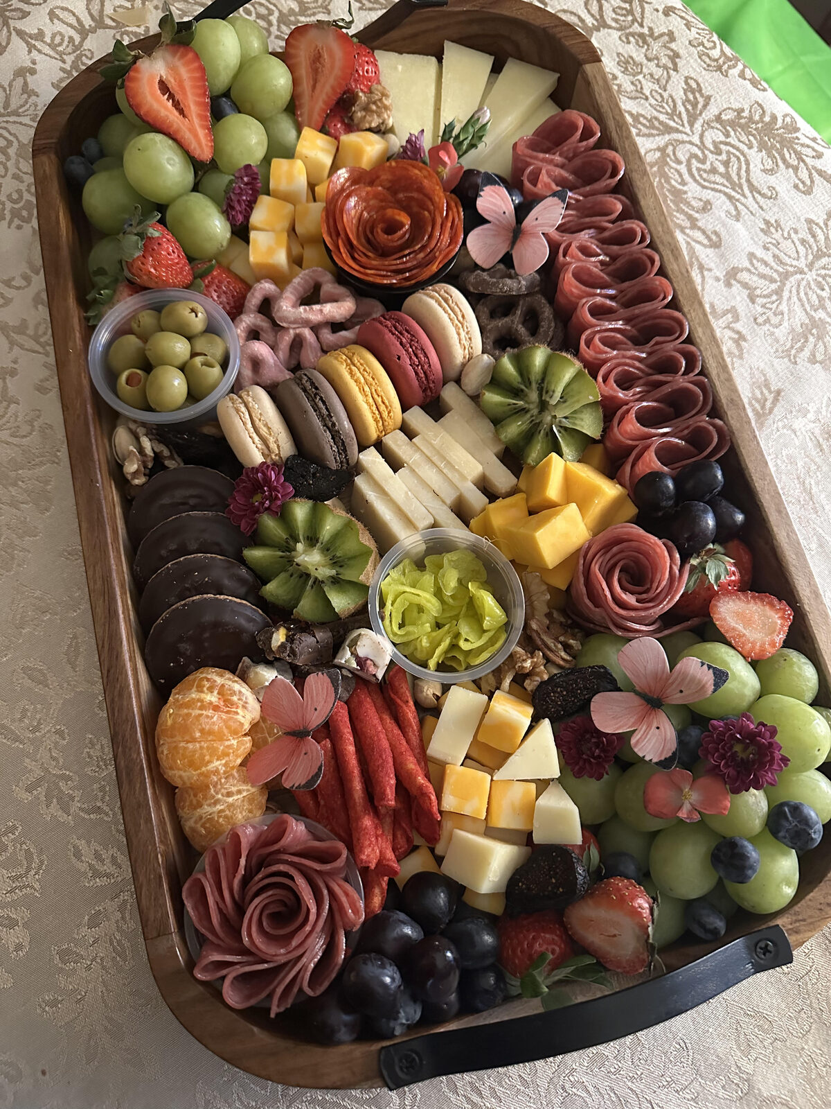 Abundant oval charcuterie board with salami roses, fruit, and macarons