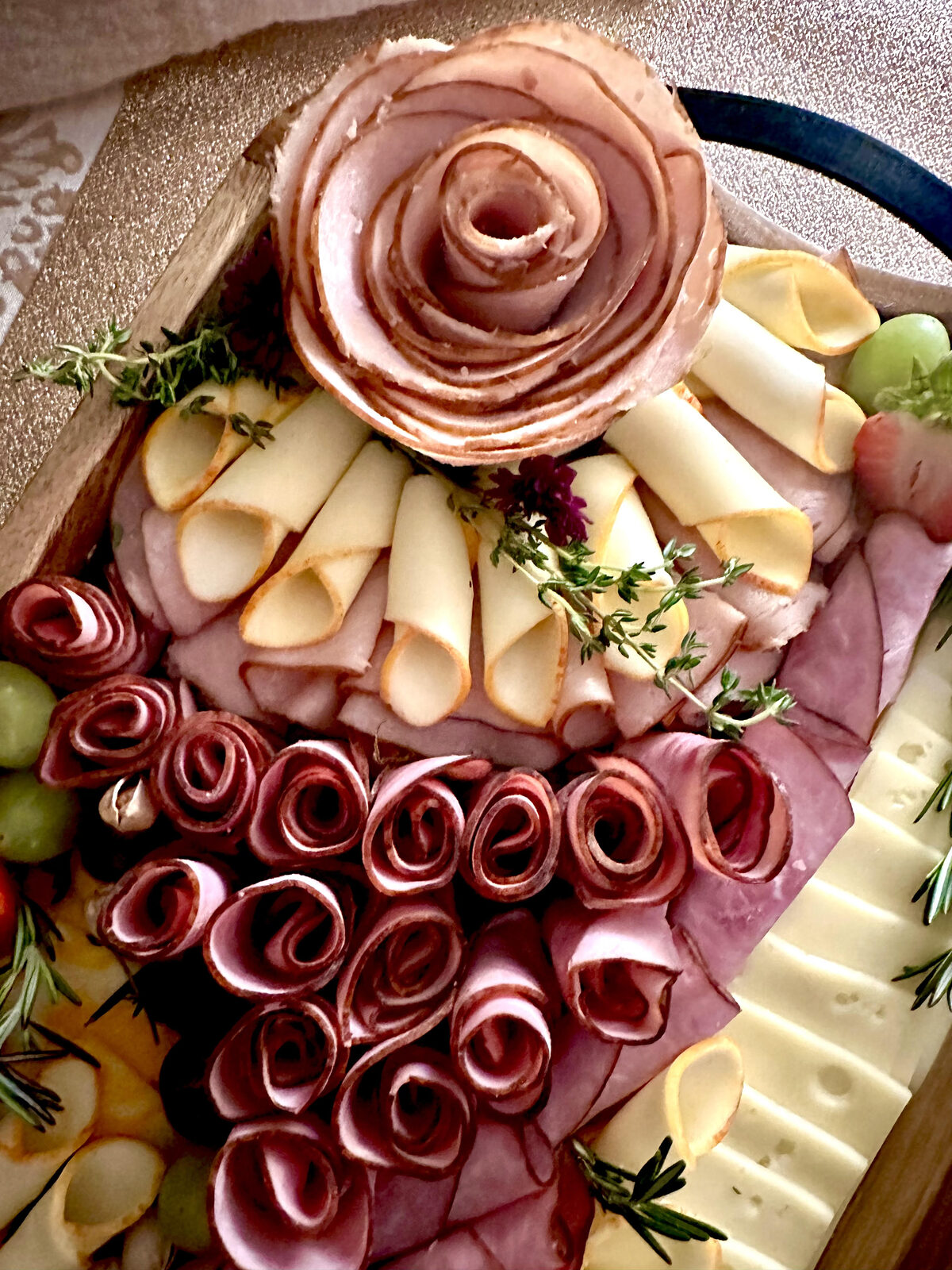 Rustic wood charcuterie board with a ham-rose centerpiece, cheeses, and salami roses
