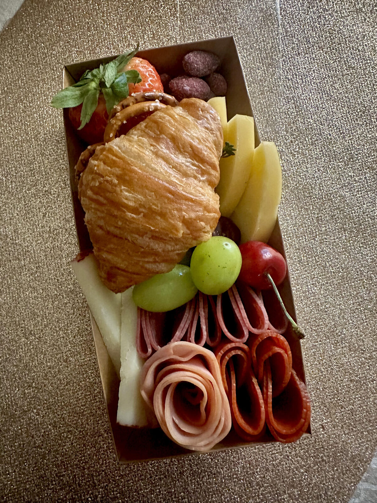 Breakfast charcuterie box with croissant, meats, and fruit