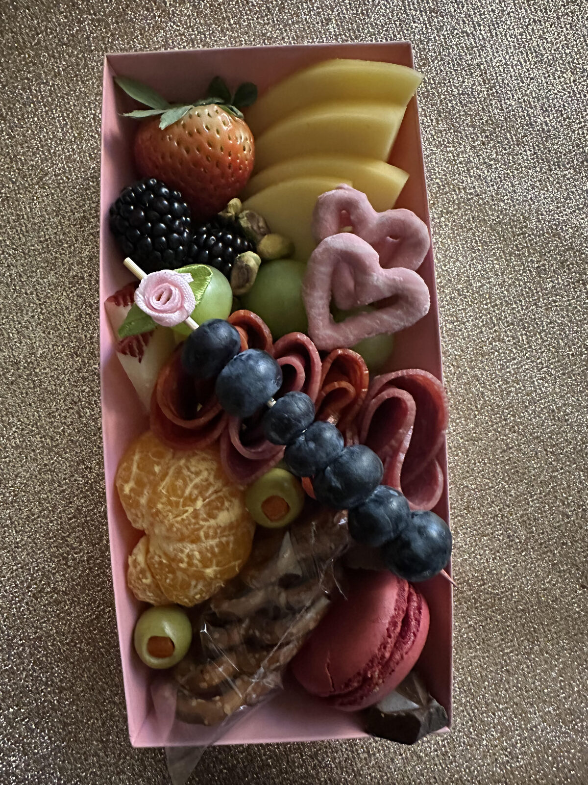 Pink box with heart-shaped salami and fruit